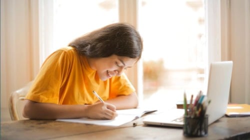 A student writes an essay instead of typing on her laptop